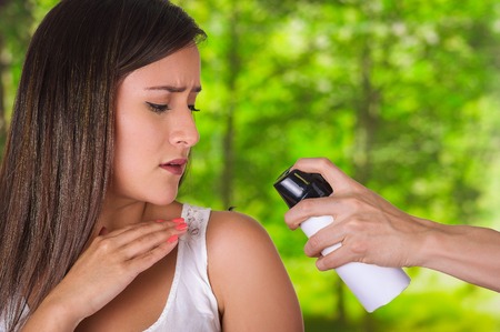 Close up of beautiful young woman looking at her shoulder while a man hand is using a spay over the insect to kill it, in a blurred backgroundの写真素材