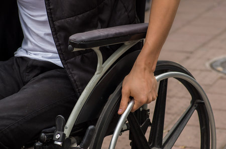 Close-up of male hand on wheel of wheelchair during walk in parkの写真素材