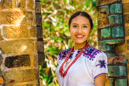 QUITO, ECUADOR - AUGUST, 30 2017: Portrait of a young indigenous woman wearing a typical andean clothes, posing for camera in front of an old wall, in the park.のeditorial素材