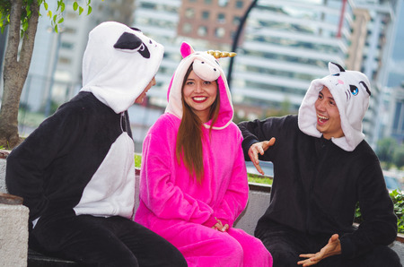 Close up of a happy group of friends having a fun conversation and wearing different costumes, one woman wearing a pink unicorn costume, other woman a panda costume and the man wearing a cat costume, in the city of Quitoの写真素材