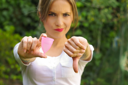 Close up of a young woman pointing in front of her a menstrual cup in one hand, Gynecology concept, ith her thums down rejecting the use of the mentrual cup, in a blurred backgroundの写真素材