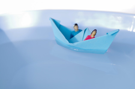 Miniature little people, couple inside of a paper boat sailing in the waterの写真素材