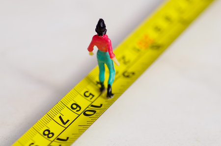 Miniature little people woman walking over a yellow tape measure isolated