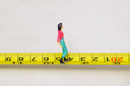 Miniature little people woman walking over a yellow tape measure isolated