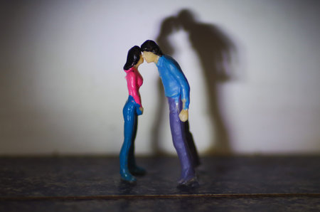 Miniature little people, couple kissing with a shadow behind
