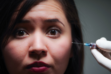 Portrait of a scary beautiful woman, with a needle injection treatment near of her faceの写真素材