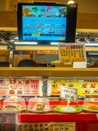 TOKYO, JAPAN -28 JUN 2017: Close up of assorted japanesse food over a table, with a screen with the menu, inside of a kaitenzushi conveyor belt sushi restaurant in Tokyoのeditorial素材