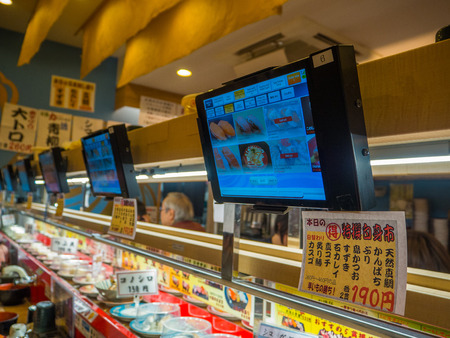 TOKYO, JAPAN -28 JUN 2017: Close up of assorted japanesse food over a table, with a screen with the menu, inside of a kaitenzushi conveyor belt sushi restaurant in Tokyoのeditorial素材