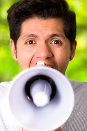 Portrait of a handsome man shouting with a megaphone in a blurred green backgroundの写真素材