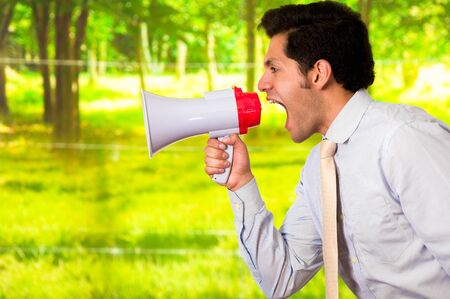 Portrait of a young man screaming with a megaphone, in a blurred green backgroundの写真素材