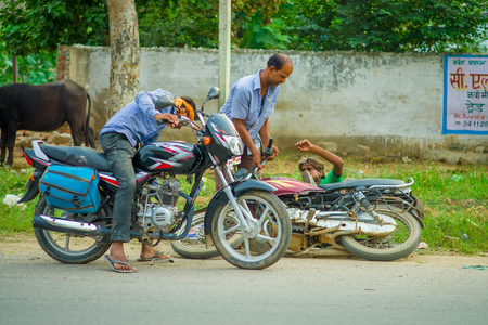 AGRA, INDIA - SEPTEMBER 19,M 2017: Unidentified man rides a motorcycle, while other man is helping his friend that felldown from his motorcycle, in the streets in central India in Agra, Indiaのeditorial素材