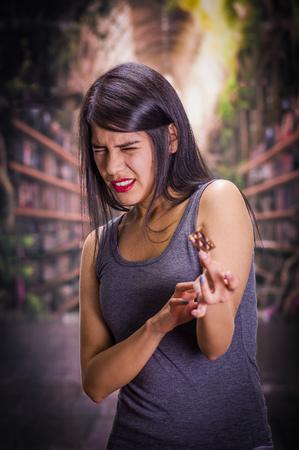 Beautiful and lonely girl suffering from anorexy, holding in her hand a piece of chocolate and doing a disgusting face, in a blurred backgroundの写真素材
