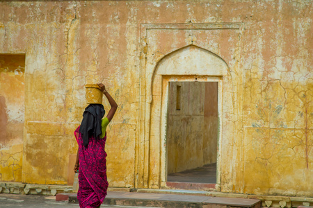 Amber, India - September 19, 2017: Close up of a woman carrying in her head a basket while she is walking inside of the city in Amber Fort on the streets of Amber, India, in a blurred yellow backgroundのeditorial素材