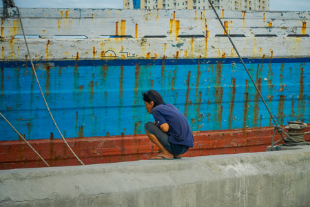 JAKARTA, INDONESIA - 3 MARCH, 2017: Man sitting down looking at water next to large fishing boatのeditorial素材
