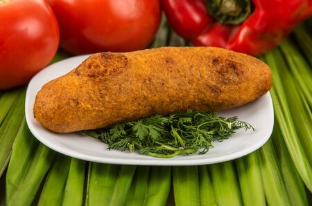 Muchin, an ecuadorian typical food on a white plate with a blurred tomato and pepper behind over a green leafの写真素材