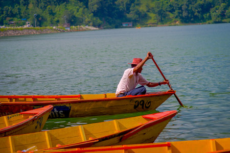 POKHARA, NEPAL - NOVEMBER 04, 2017: Close up up of man paddling the yellow boat at Begnas lake in...