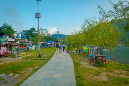 Pokhara, Nepal - September 04, 2017: Unidentified people wlaking in the stoned lakeshore with some...