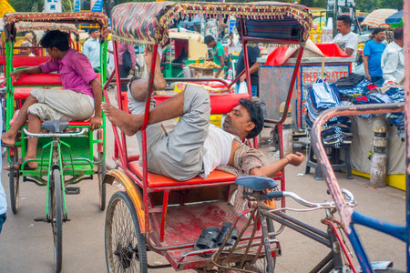 DELHI, INDIA - SEPTEMBER 25 2017: Unidentified man resting over his red Rickshaws in the streets in...