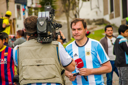 QUITO, ECUADOR - OCTOBER 11, 2017: Close up of reporter talking to some ecuadorian fans surrounding with a crowd of people wearing official Marathon football shirt, screaming and jumping supporting his teamのeditorial素材
