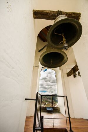 QUITO, ECUADOR - MAY 06 2016: Close up of three huge bells inside of a bulding in the San Francis church, with a town buildings behind in the city of Quitoのeditorial素材