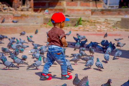 KATHMANDU, NEPAL - April 26, 2012: Unidentified little black child walking in the street with a flock of pigeons, at Durbar square near old hindu temples in Kathmandu, Nepalのeditorial素材