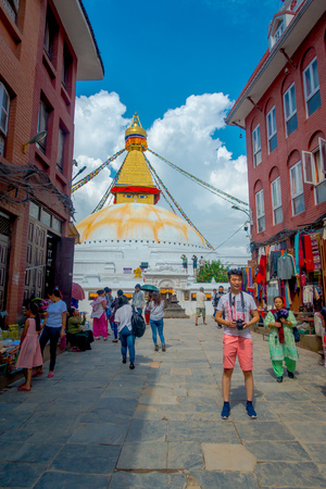 KATHMANDU, NEPAL OCTOBER 15, 2017: Unidentified people walking in the streets between some buildings and enjoying the beautiful monument of Boudhanath stupa and its colorful flags in daylight with bue sky, in Kathmandu, Nepal.のeditorial素材