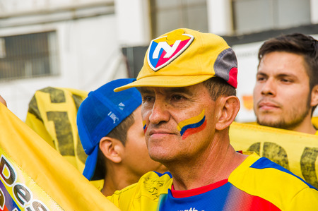 QUITO, ECUADOR - OCTOBER 11, 2017: Portrait of old man wearing a yellow hat with his face painted with the colors of Ecuador, yellow, blue and red and wearing official Marathon football shirtのeditorial素材