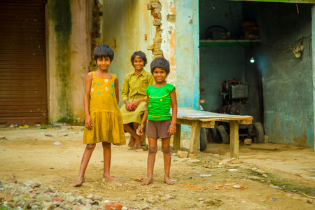 Agra, India - September 20, 2017: Portrait of children, wearing a yellow dirty blouse and a green t-shirt and brown pants and, over a stoned ground, in the street in Agra city in Indiaのeditorial素材