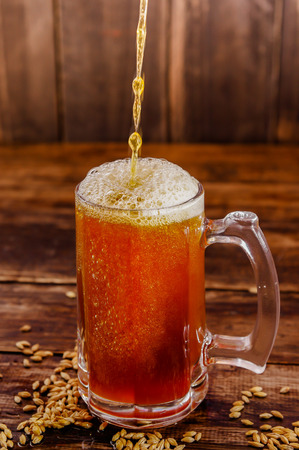Indoor view of filling a glass of beer, and wheat in the base on a wooden table backgroundの写真素材