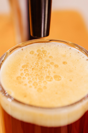 Close up of a glass of beer with foam and beer tap pouring, beer serving in a restaurant or pub, in a blurred backgroundの写真素材