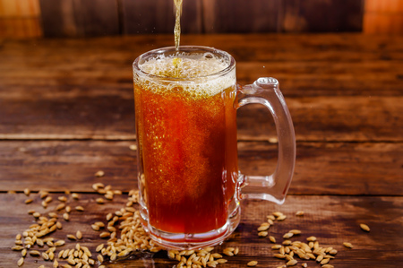 Indoor view of glass of beer with wheat in the base on a wooden table on a dark pubの写真素材