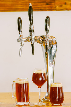 Close up of multiple beer taps located over a wooden table with some glasses full of beer, in a blurred backgroundの写真素材