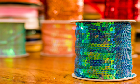 Cose up of shiny rolls of colorful sequins green tape, multi-colored over a wooden table in a blurred backgroundの写真素材