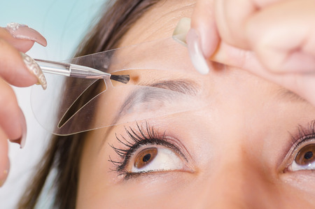 Close up of young beautiful woman doing a mess in her eyebrow in a blurred backgroundの写真素材