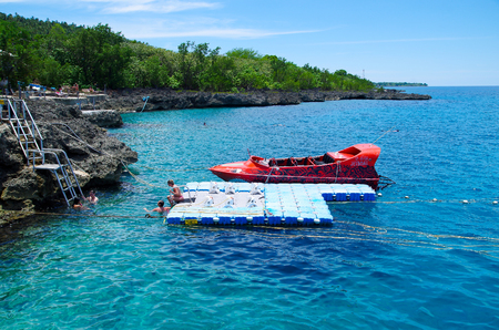 WEST VIEW, COLOMBIA - OCTOBER 03, 2017: Outdoor view of a red boat and unidentified people swimming and enjoying the beautiful blue water, San Andres Island from west view during a sunny day in San Andres, Colombiaのeditorial素材