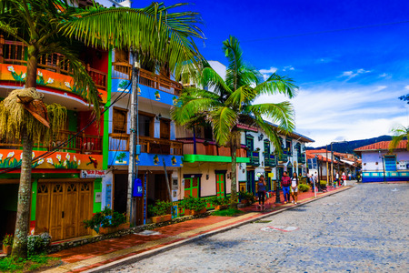 GUATAPE, COLOMBIA - OCTOBER 19, 2017: Unidentified people walking in a beautiful decorated buildings of Guatape city with some palms trees, near Medellin, Antioquia, Colombiaのeditorial素材