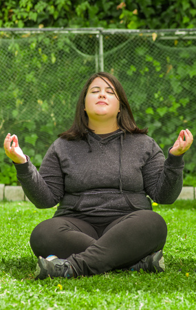 Young woman doing yoga exercise at outdoors, lotus pose meditation in a garden backgroundの写真素材