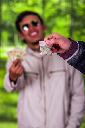Close up of a man addict and dealer trafficking, addict with money buying dose from dealer with drugs, in a blurred backgroundの写真素材