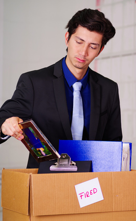 Close up of sad man packing his belongings after being fired from his job in a blurred backgroundの写真素材