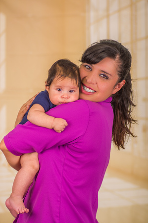 Close up of young mother is holding her little baby, mom wearing a purple blouse and baby blue clothes, in a blurred backgroundの写真素材