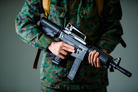 Close up of soldier holding a rifle with both hands and wearing a military uniform, in a gray...