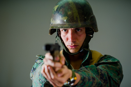 Portrait of a young soldier pointing a gun in gray backgroundの写真素材