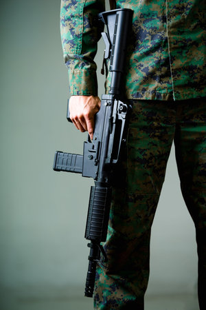 Close up of soldier holding a rifle, wearing a military uniform, in a gray background