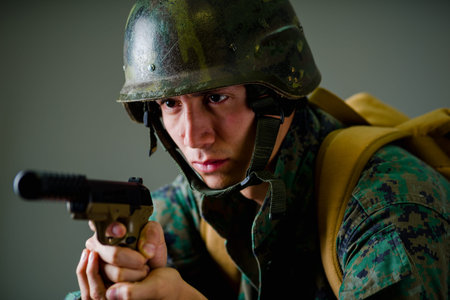 Portrait of a young soldier pointing a gun in gray backgroundの写真素材