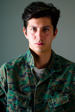 Portrait of a serious young soldier wearing a military uniform, a packpack in a gray backgroundの写真素材