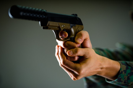 Indoor view of a soldier holding with both hands a gun in gray backgroundの写真素材