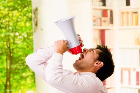 Close up of a handsome man screaming with a megaphone, pointing to the sky in a blurred backgroundの写真素材