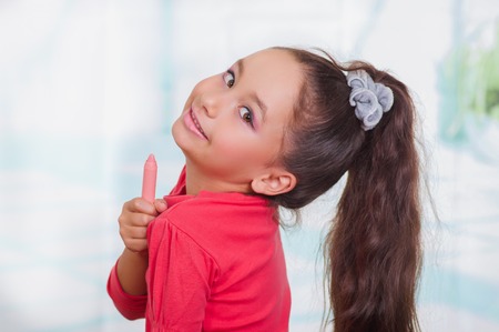 Close up of little beautiful girl holding in her hands a lipstick in a blurred backgroundの写真素材