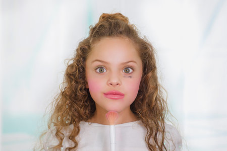 Close up of little surprised beautiful girl using wrong a brush to make up in a blurred backgroundの写真素材