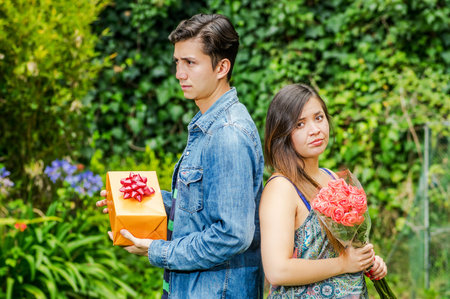 Close up of mad woman holding flowers and mad man holding a gift back to back ignoring each other,...